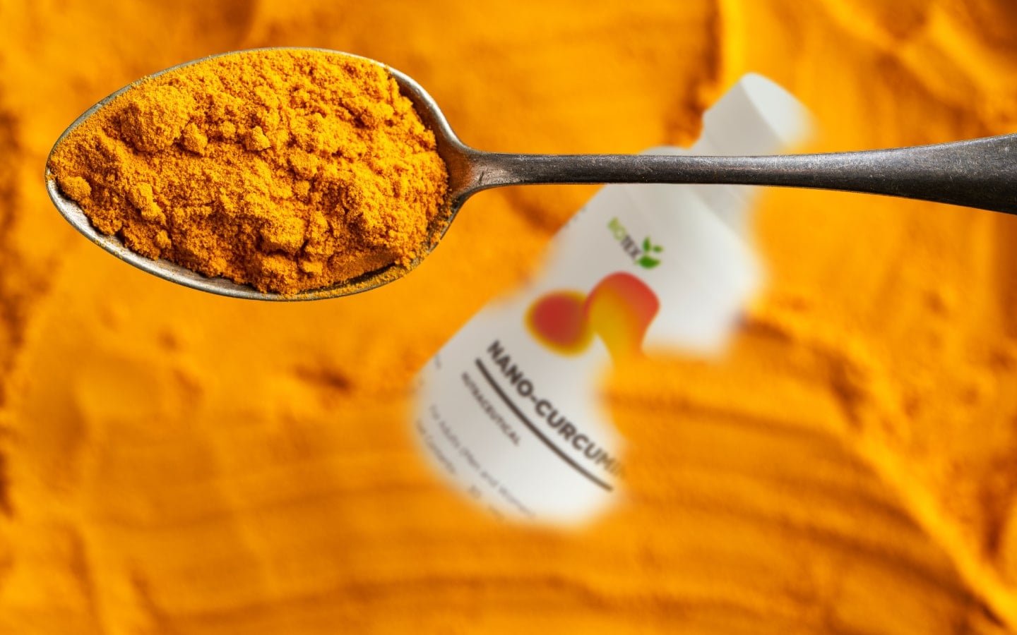 Spoon full of turmeric powder over a blurred supplement bottle