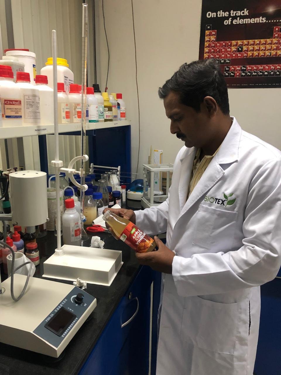 Male researcher wearing a white lab coat inspecting a bottle of Apple Cider Vinegar